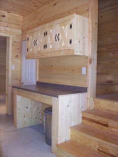 a kitchen with wooden walls and stairs leading up to the upper floor, next to a trash can