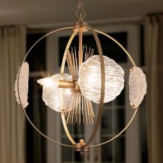 a chandelier hanging from a ceiling in a living room with curtains on the windowsill