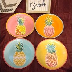 four plates with pineapples painted on them are sitting next to a sign that says, welcome to the beach