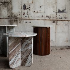 two marble tables sitting next to each other in front of a white wall with peeling paint on it