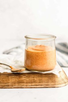 a small glass jar filled with peanut butter on top of a wooden cutting board next to a spoon