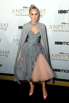 a woman in a gray dress and cape on the red carpet at an awards event