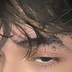 a close up of a person's face with black hair and piercings on his forehead