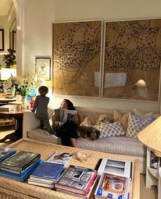 two people are sitting on a couch with their dog in front of them and there is a coffee table full of books