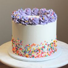 a white cake with purple frosting and sprinkles on top sitting on a table