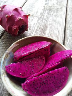 purple fruit is sitting on a plate next to a piece of red fruit that has been cut in half