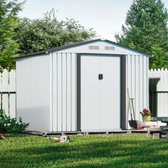 a white shed sitting on top of a lush green field next to a fence and trees