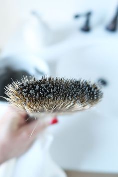 a person holding a brush in their hand near a sink and faucet with water running down it