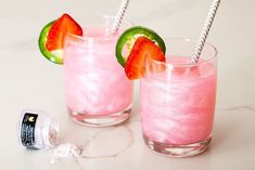 two glasses filled with pink liquid and topped with strawberries, kiwis and lime