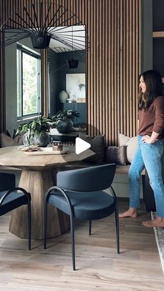 a woman standing in front of a table with chairs and a mirror on the wall