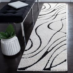 a black and white rug in a living room next to a bench with a plant on it