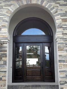 the front entrance to a home with arched glass doors and brick pillars, along with stone steps