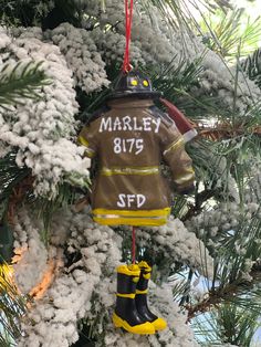 a fireman's jacket ornament hanging from a christmas tree with snow on it