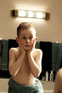 a young boy sitting in front of a bathroom mirror with his hands on his face