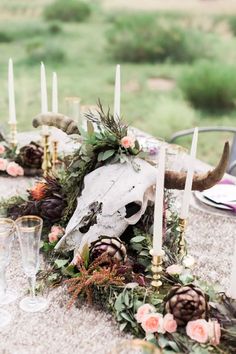 a table with candles, flowers and an animal's skull decorated with greenery