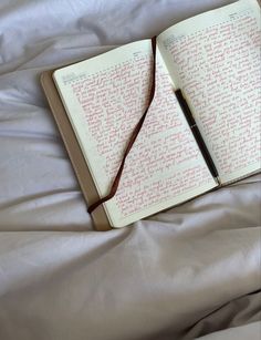 an open book with writing on it laying on a bed next to a pen and pillow