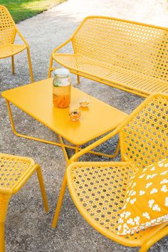 yellow chairs and tables are sitting outside on the cement ground with a jar of orange juice