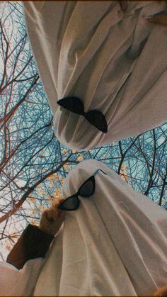 two pairs of sunglasses hanging from the side of white curtains with trees in the background