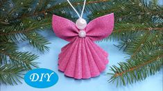 an ornament made out of pink paper with a pearl in the center on a pine branch