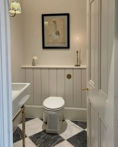 a white toilet sitting inside of a bathroom next to a sink under a framed painting