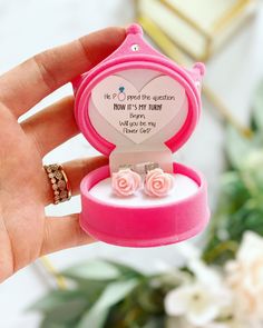 a person holding a pink ring box with two small roses in it and a quote on the inside