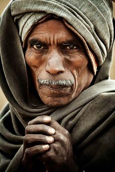 an old man wearing a turban and holding his hands to his chest, looking at the camera