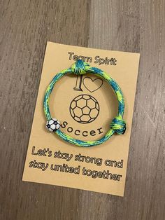 a bracelet with a soccer ball on it sitting on top of a wooden table next to a card