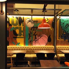 the interior of a restaurant with wooden tables and chairs, artwork on the wall behind them