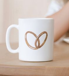 a white coffee mug with two gold rings on it sitting on top of a wooden table