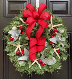 a christmas wreath with red bow hanging from the front door, decorated with holly and starfish