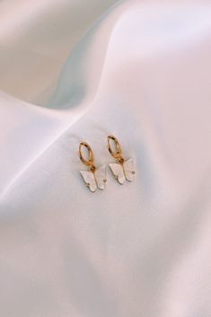 Elegant Pearlescent Butterfly Huggie Earrings. Hoops are made of gold plated brass, and each dainty butterfly charm is made of a pearlescent pewter acrylic, with a gold or rhodium backing. Dainty Gold-plated Butterfly Jewelry, White Dainty Gold-plated Hoop Earrings, Dainty Gold Plated Butterfly Jewelry, White Gold Plated Dainty Hoop Earrings, Dainty Yellow Gold Earrings With Butterfly Charm, White Dainty Butterfly Earrings, Dainty White Butterfly Earrings, Dangle Hoop Earrings With Butterfly Charm As A Gift, Delicate Gold Earrings With Butterfly Charm