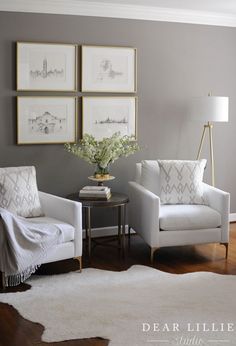 a living room with two white chairs and pictures on the wall