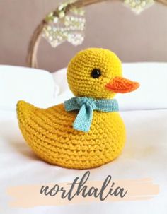 a crocheted yellow duck with a blue bow on its head sitting on a bed