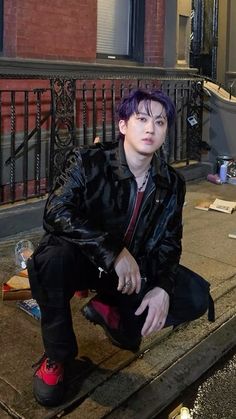 a man with purple hair sitting on the sidewalk