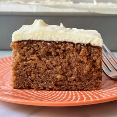 a slice of carrot cake with cream cheese frosting on an orange plate next to a fork