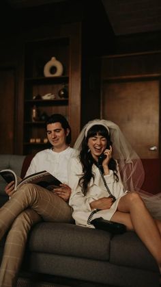 a bride and groom are sitting on a couch talking on their cell phones while they smile at each other