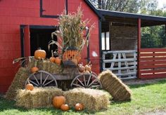 hay bales and pumpkins in front of a red barn with an old fashioned wagon