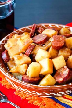 a bowl filled with potatoes and sausage on top of a red table cloth next to a fork