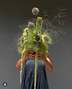 a woman is holding a large green plant in front of her face and covering her eyes