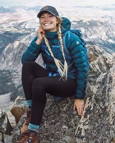 a woman sitting on top of a mountain with long braids and wearing a blue jacket