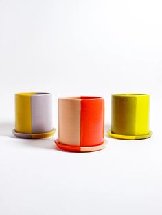 three different colored cups sitting next to each other on a white surface with one yellow cup in the middle