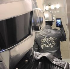 a man wearing a leather jacket taking a selfie in front of a motorcycle helmet