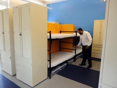 a man standing next to bunk beds in a room with blue walls and white cupboards