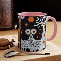 a pink and black coffee mug sitting on top of a wooden table next to a cookie