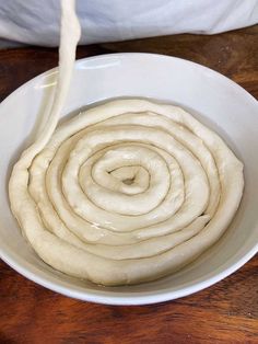 a white bowl filled with dough on top of a wooden table