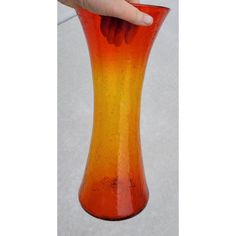 a hand is touching an orange vase with yellow and red highlights on it's surface