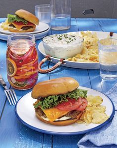 there is a sandwich and chips on the blue picnic table with water in glass bottles