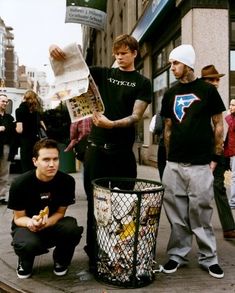 a group of young men standing next to each other near a trash can on a city street