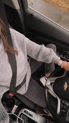 a woman sitting in the driver's seat of a car with her hand on the steering wheel