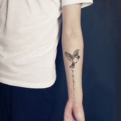 a person with a small tattoo on their arm holding a flower in one hand and a bird in the other